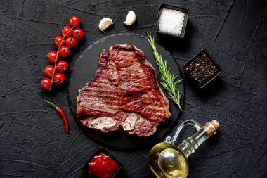 Baharatlı çiğ biftek ve siyah arka planda otlar.