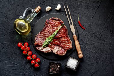 Baharatlı çiğ biftek ve siyah arka planda otlar.