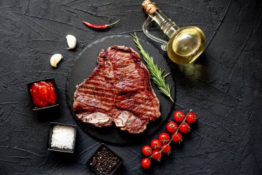 Baharatlı çiğ biftek ve siyah arka planda otlar.