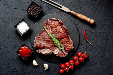 Baharatlı ızgara biftek ve siyah arka planda otlar.