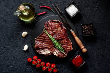 Baharatlı çiğ biftek ve siyah arka planda otlar.