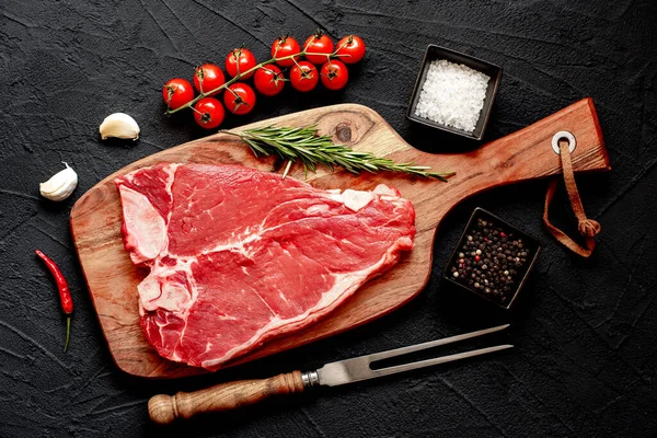 Baharatlı çiğ biftek ve siyah taş arka planda otlar. en üstteki görünüm.