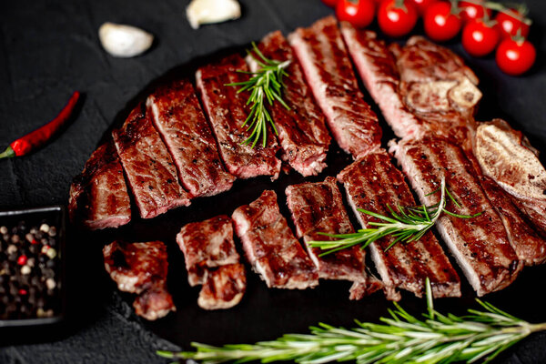 Close up of sliced grilled beef steak with spices and rosemary on black background