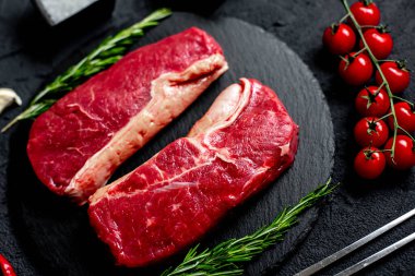 Baharatlı çiğ biftek ve siyah taş arka planda otlar.