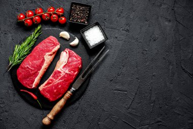 Baharatlı çiğ biftek ve siyah taş arka planda otlar.