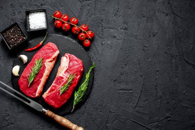 Baharatlı çiğ biftek ve siyah taş arka planda otlar.