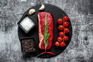Baharatlı çiğ biftek ve siyah taş arka planda otlar.