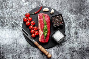 Baharatlı çiğ biftek ve siyah taş arka planda otlar.