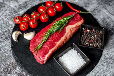 Baharatlı çiğ biftek ve siyah taş arka planda otlar.