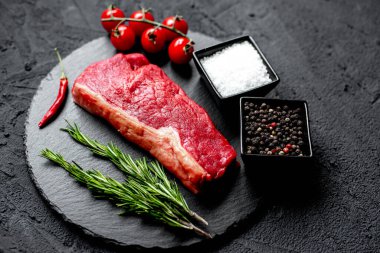 Baharatlı çiğ biftek ve siyah taş arka planda otlar.