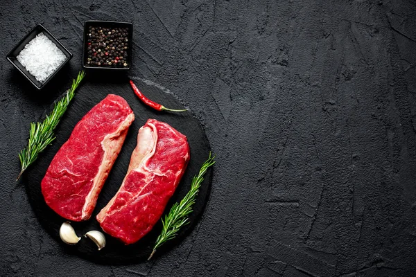 stock image raw beef steak with spices and herbs on black stone background