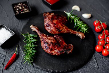 grilled chicken legs with spices and herbs on black background