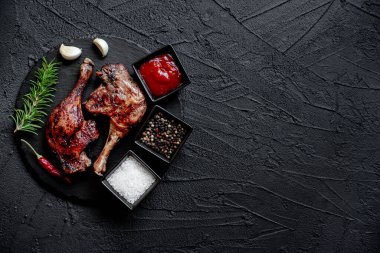 grilled chicken legs with spices and herbs on black background