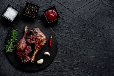 grilled chicken legs with spices and herbs on black background
