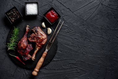 grilled chicken legs with spices and herbs on black background