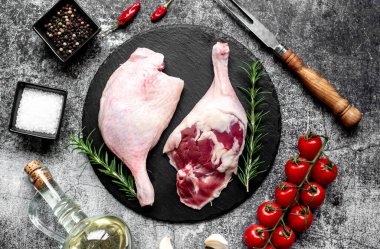 Çiğ ördek bacakları, otlar ve baharatlarla taştan arka planda.