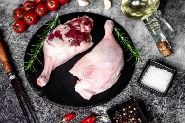 Çiğ ördek bacakları, otlar ve baharatlarla taştan arka planda.