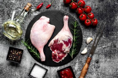 Çiğ ördek bacakları, otlar ve baharatlarla taştan arka planda.