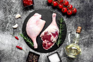 Çiğ ördek bacakları, otlar ve baharatlarla taştan arka planda.