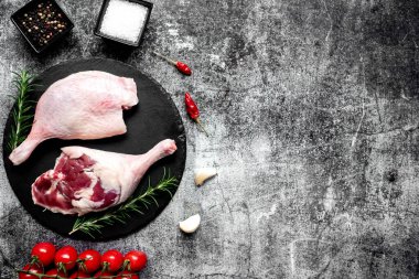 Çiğ ördek bacakları, otlar ve baharatlarla taştan arka planda.