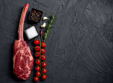 Çiğ Tomahawk bifteği ve baharatları siyah taş arka planda.