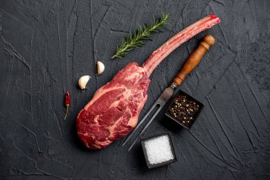 Çiğ Tomahawk bifteği ve baharatları siyah taş arka planda.