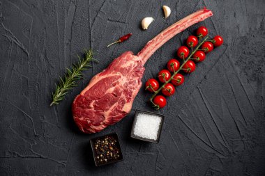 Çiğ Tomahawk bifteği ve baharatları siyah taş arka planda.