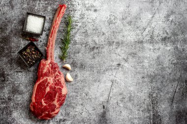 Çiğ Tomahawk bifteği ve baharatları gri taş arka planda.