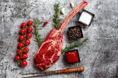 Çiğ Tomahawk bifteği ve baharatları gri taş arka planda.
