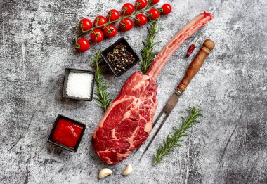 Çiğ Tomahawk bifteği ve baharatları gri taş arka planda.