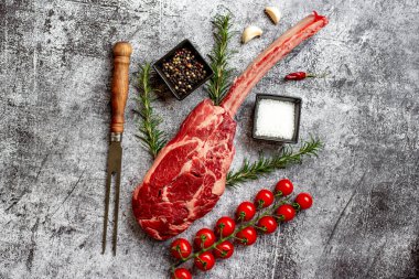 Çiğ Tomahawk bifteği ve baharatları gri taş arka planda.