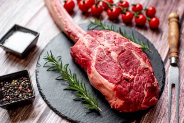 Tomahawk bifteği ve baharatları ahşap masa arkasında.