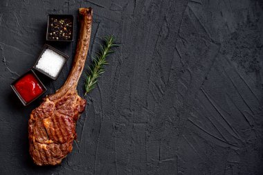 Siyah taş arka planda ızgara Tomahawk bifteği ve baharatları.