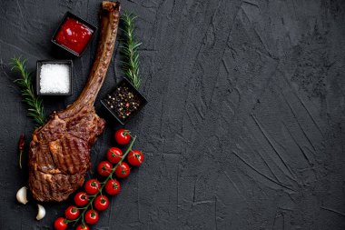 Siyah taş arka planda ızgara Tomahawk bifteği ve baharatları.