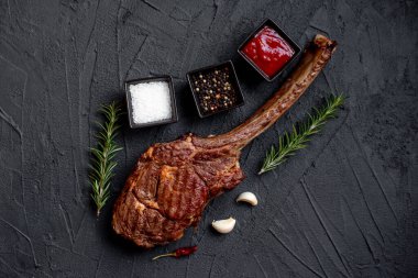 Siyah taş arka planda ızgara Tomahawk bifteği ve baharatları.