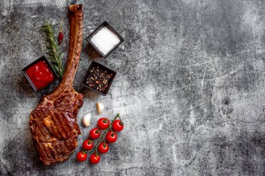 Gri taş arka planda ızgara Tomahawk bifteği ve baharatları.