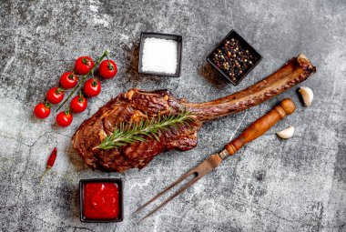 Gri taş arka planda ızgara Tomahawk bifteği ve baharatları.