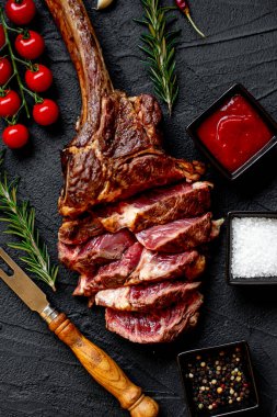 Siyah taş arka planda ızgara Tomahawk bifteği ve baharatları.