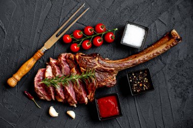 Siyah taş arka planda ızgara Tomahawk bifteği ve baharatları.