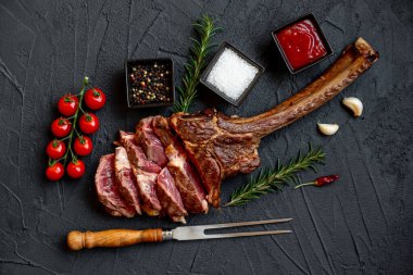 Siyah taş arka planda ızgara Tomahawk bifteği ve baharatları.