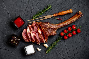 Siyah taş arka planda ızgara Tomahawk bifteği ve baharatları.
