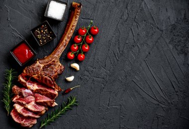 Siyah taş arka planda ızgara Tomahawk bifteği ve baharatları.