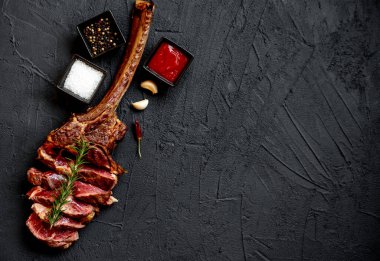 Siyah taş arka planda ızgara Tomahawk bifteği ve baharatları.