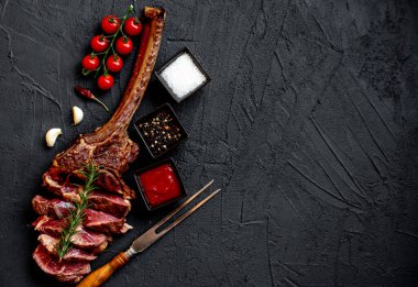 Siyah taş arka planda ızgara Tomahawk bifteği ve baharatları.