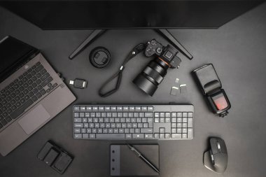Karanlık arka planda çalışan fotoğrafçı bilgisayarı, kamerası, flaşı, lensi, tableti, klavyesi, faresi var. Üst görünüm