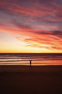 Gün doğarken kumsalda kolları açık olan biri. Dikey fotoğrafçılık