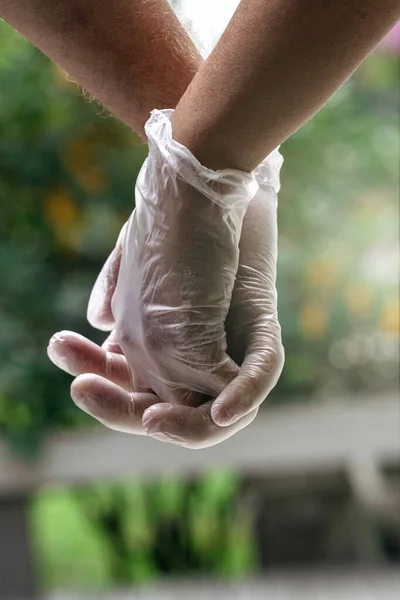 Close up caption of two hands with sanitary gloves holding each other. Vertical photography