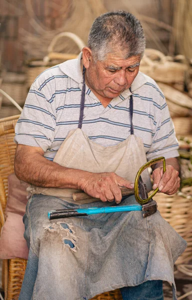 Latin old man using hammer for making wicker baskets at his workshop. Vertical photography