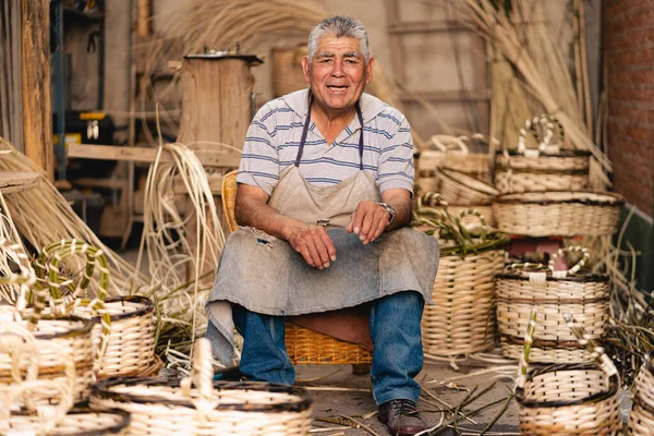 Latin American mature artisan smiling and looking at camera in his wicker workshop. Latin American culture and tradition concept