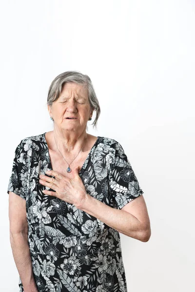 Old woman suffering heart pain and gesturing with eyes closed over isolated white background. Vertical photography